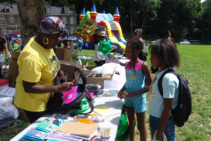 A woman at a table hands out school supplies to children at a community event.
